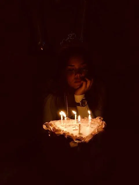 Birthday Sad Shayari showing a woman sitting alone with a candle on a dark birthday evening