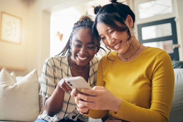 Funny Shayari On Girls Attitude showing cheerful friends laughing together while using a smartphone