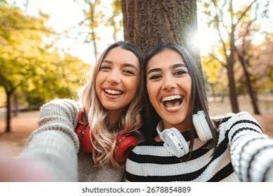 Funny Shayari On Girls Attitude showing two young women taking a playful selfie outdoors with smiles