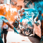 Holi Sad Shayari In Hindi showing people celebrating Holi with colorful powders and a festive street atmosphere