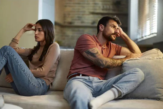 Husband Wife Sad Shayari showing a couple sitting apart on a sofa with sadness and emotional distance