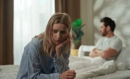Husband Wife Sad Shayari showing a married couple sitting apart on a bed after a painful disagreement