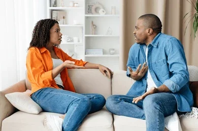 Husband Wife Sad Shayari showing a young married couple sitting apart on a sofa after an argument