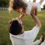 Papa Beti Shayari showing a father lifting his smiling daughter during playful outdoor time in a sunny park