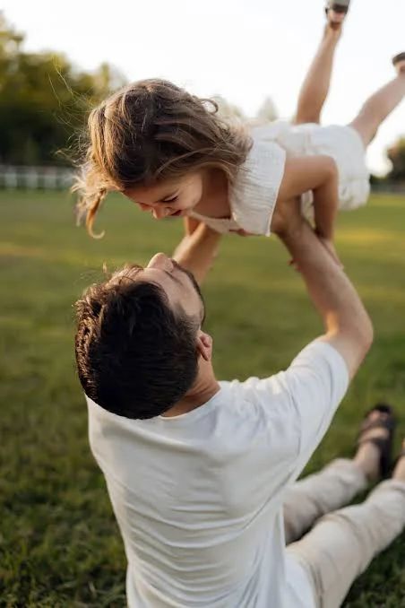 Papa Beti Shayari showing a father lifting his smiling daughter during playful outdoor time in a sunny park